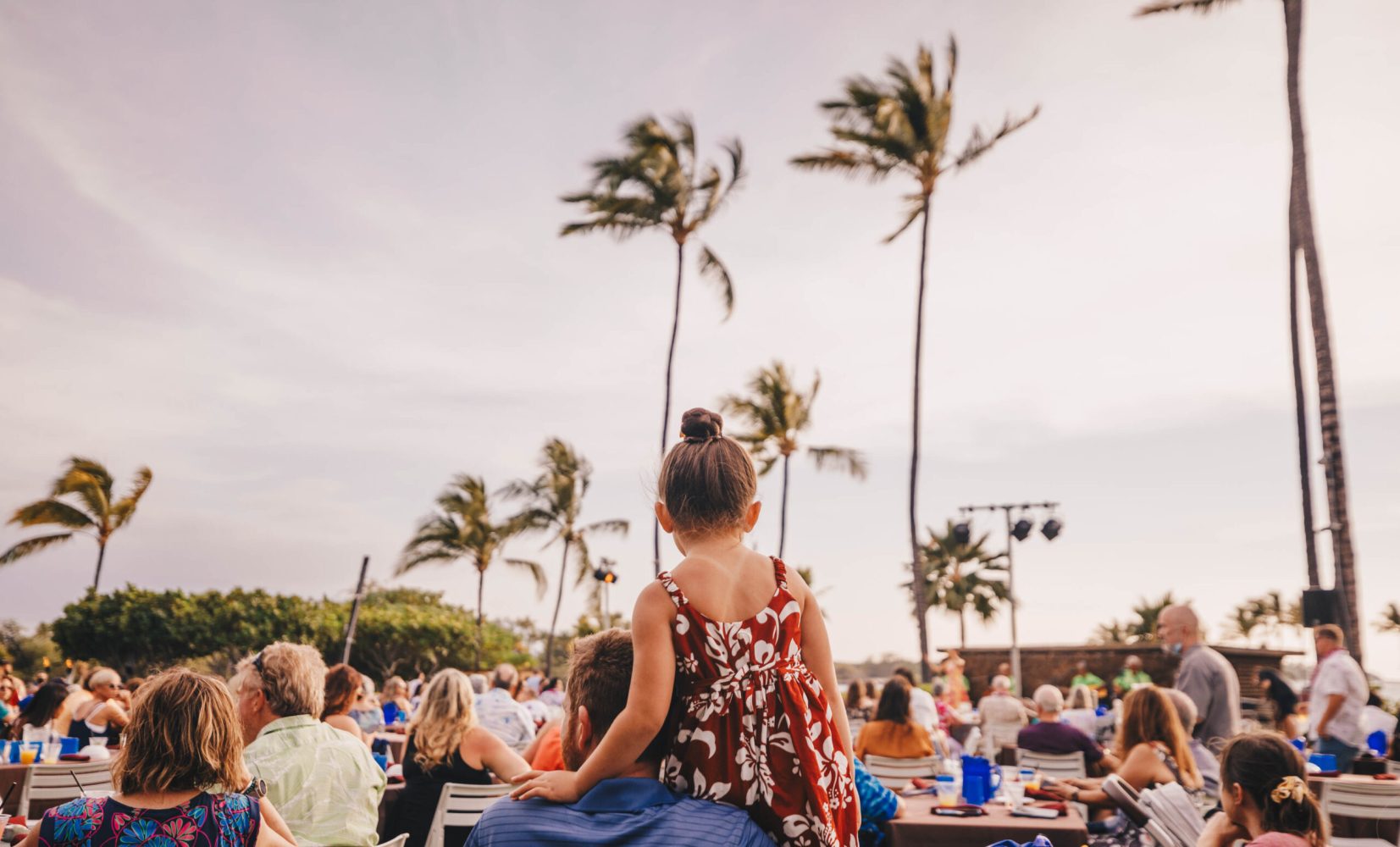 a child on her father's head looking at the luau performance